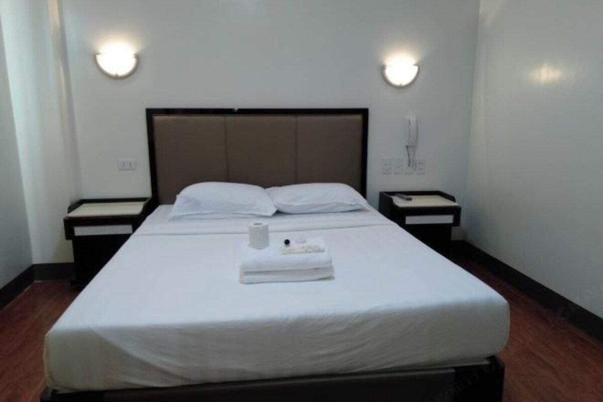 Une chambre d’hôtel avec un lit simple, deux tables de chevet et deux lampes fixées au mur.