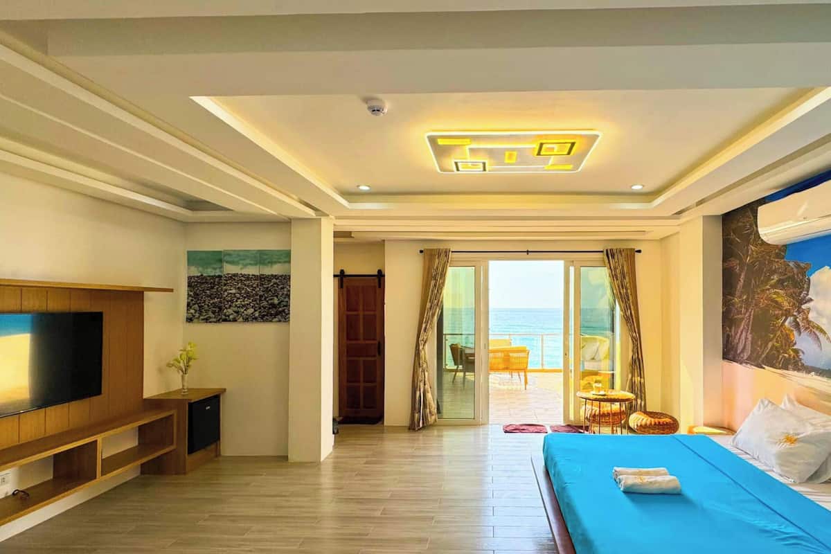 Habitación de hotel con televisión, cama, un cuadro de playa y vista al océano.