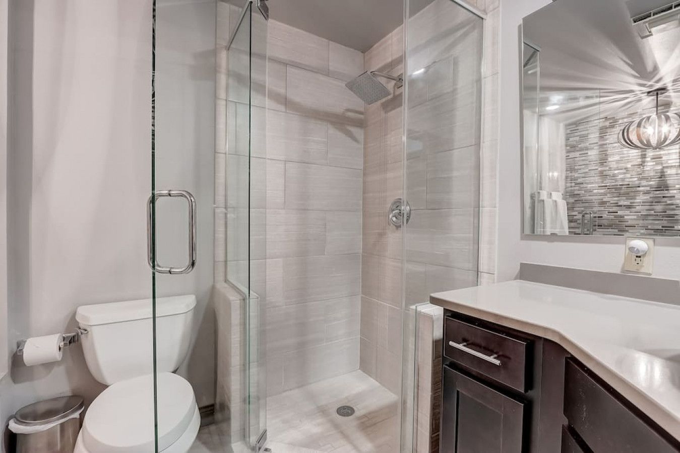 A modern bathroom with a glass-enclosed shower, a toilet, and a vanity with a mirror.