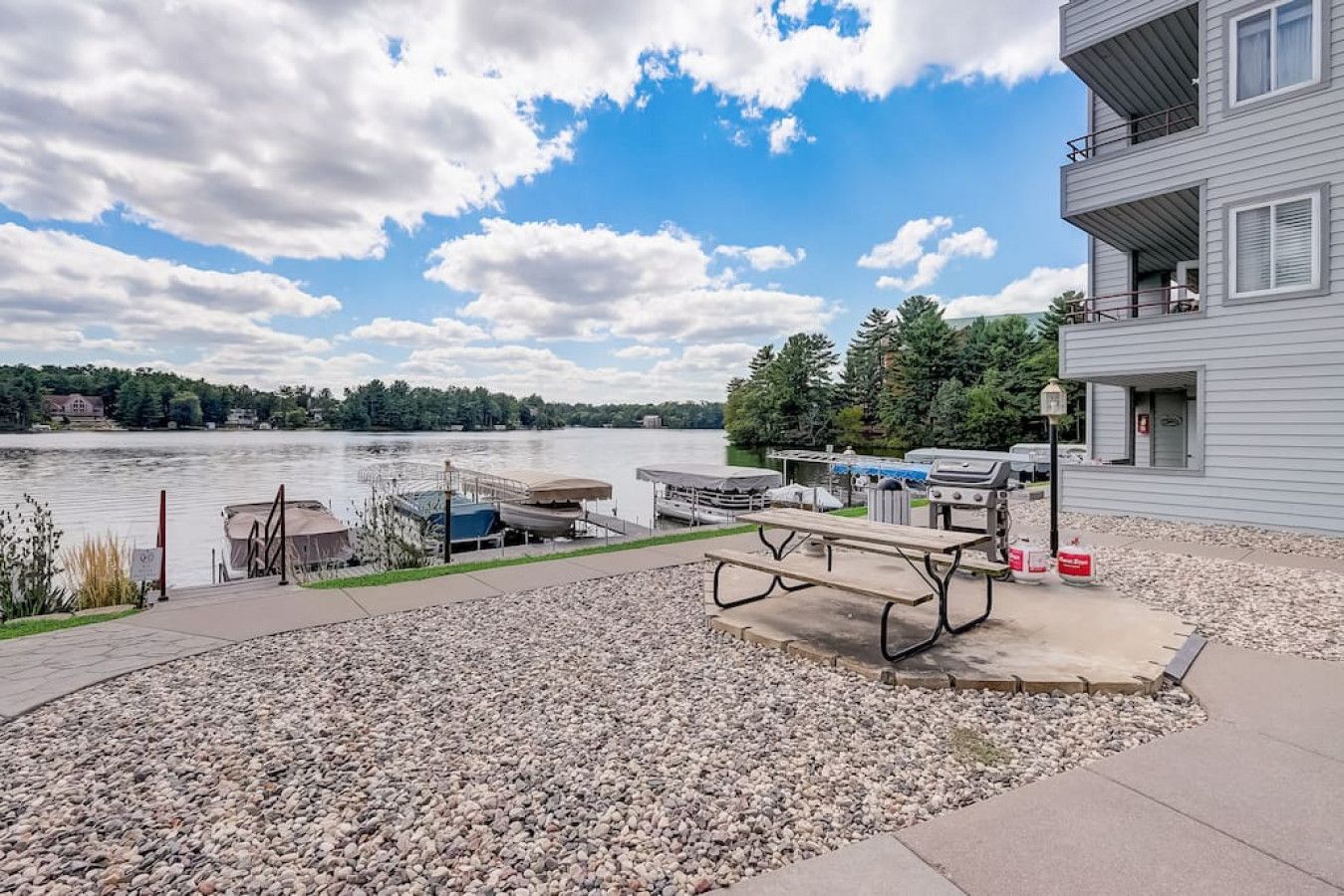 A lakeside patio with a picnic table, grill, and dock area.