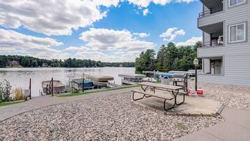 A lakeside patio with a picnic table, grill, and dock area.