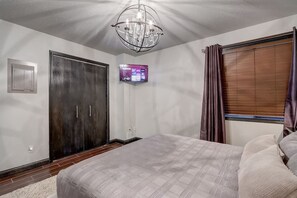 A bedroom with a large bed, a dark wooden wardrobe, a wall-mounted TV, and a window with curtains.