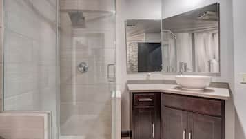 Un baño moderno con ducha de vidrio, un espejo grande y un tocador de madera oscura con lavamanos blanco.