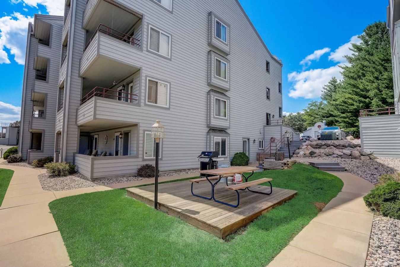 A multi-story apartment building with a well-maintained lawn, a picnic table, and a barbecue grill in the front yard.