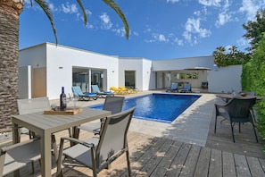 Uma área moderna de piscina ao ar livre com um deck de madeira, espreguiçadeiras e uma mesa de jantar.