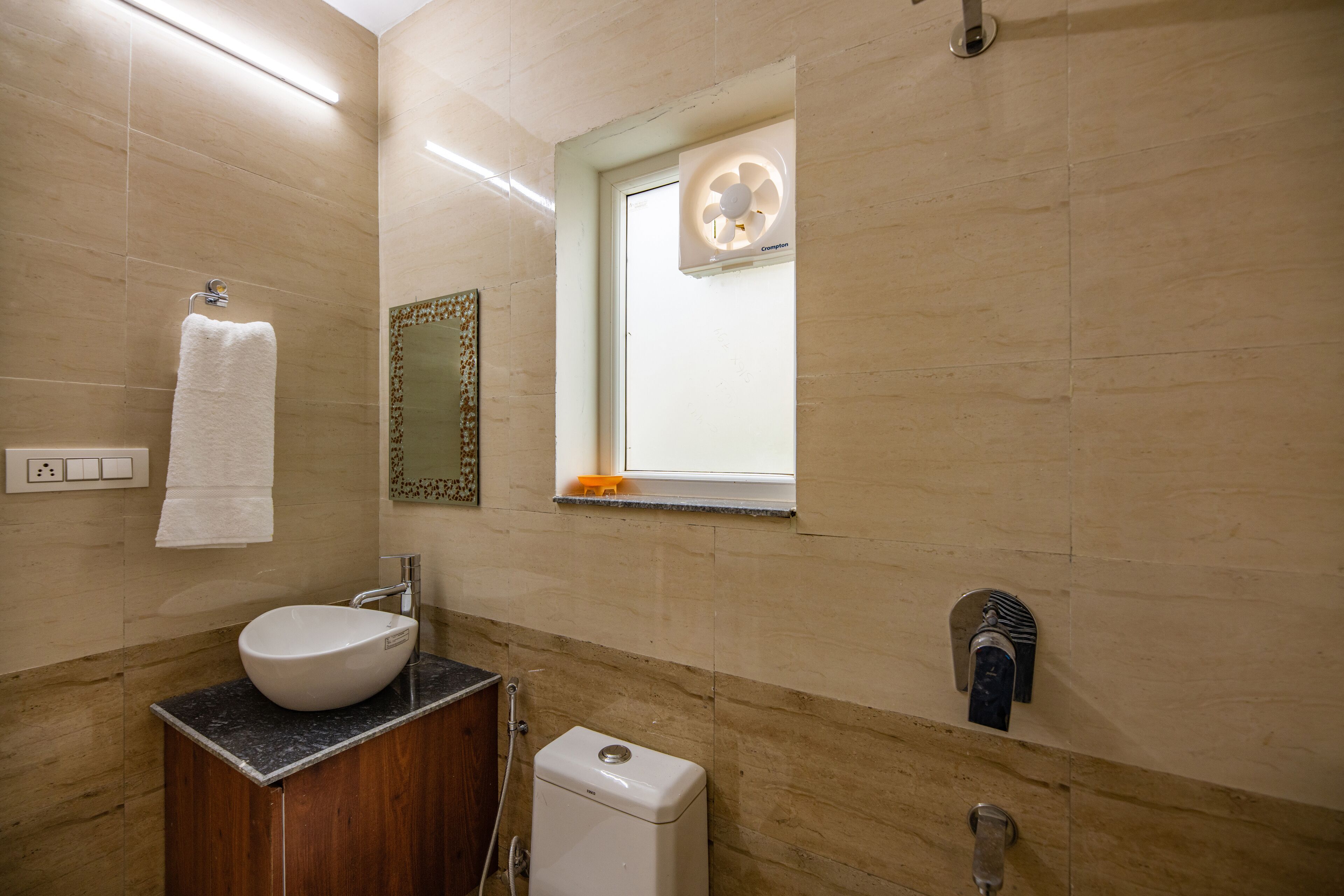 A bathroom with a white sink, a towel rack, a window with a fan, and a mirror.