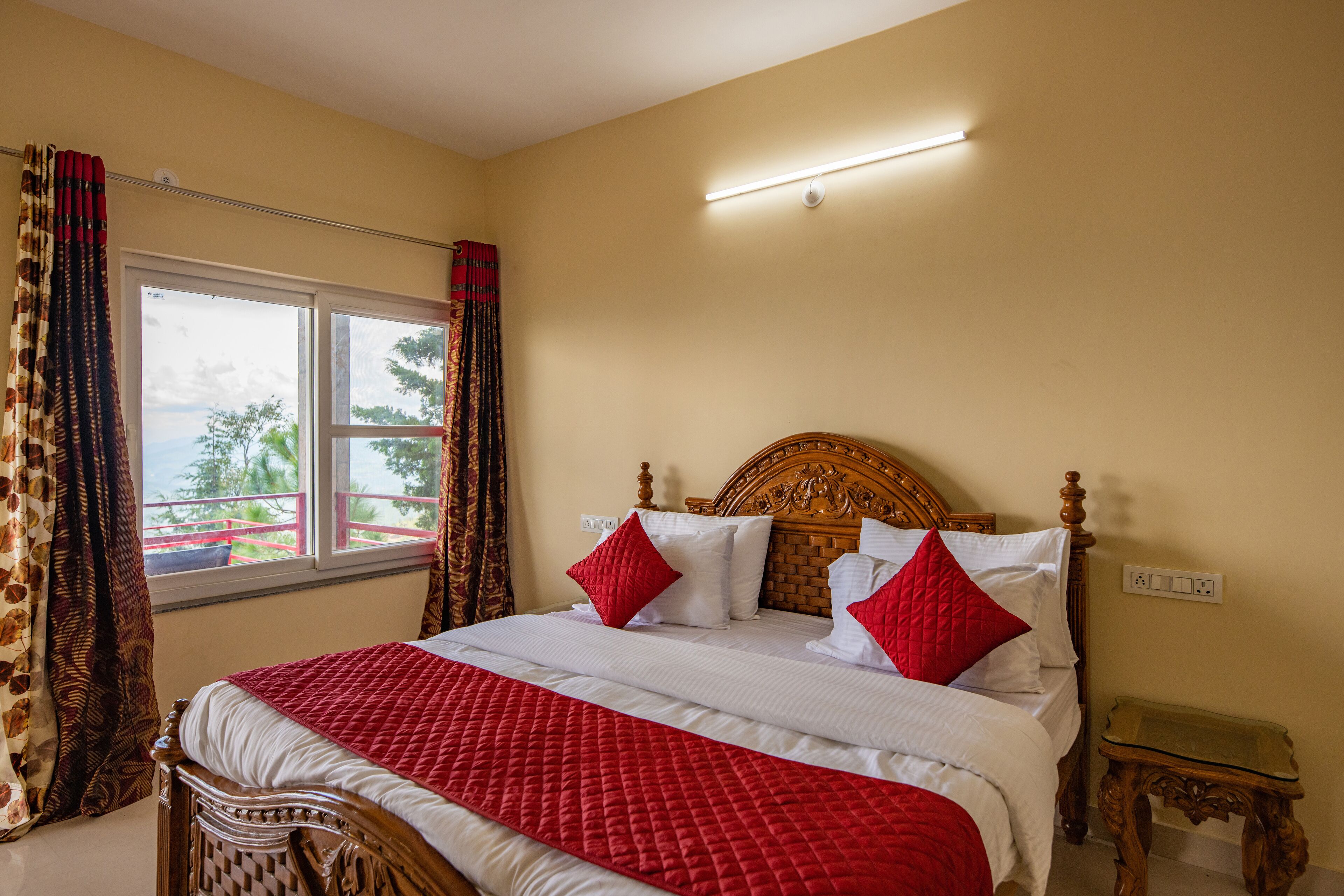 A neatly made bed with a red and white quilt, a wooden headboard, and a window with curtains.
