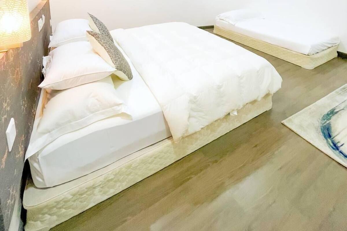 A bedroom with a bed, a bedside table, a TV mounted on the wall, and a small window.