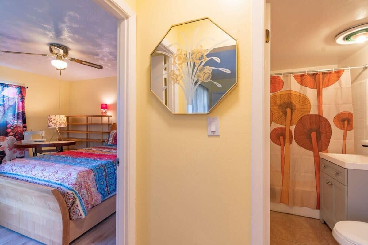 A bedroom with a bed, a desk, a chair, a ceiling fan, and a bathroom with a shower curtain.