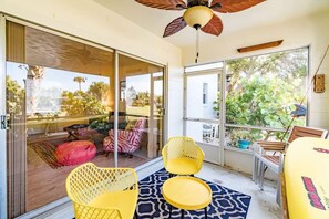 A room with a glass door leading to a balcony, yellow chairs, a small table, and a ceiling fan.