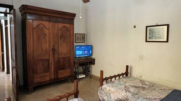 Un dormitorio con dos camas de madera, un armario de madera, un ventilador de techo, una máquina de coser y un televisor.