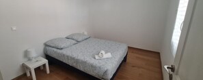 A small, neatly arranged bedroom with a bed, a bedside table with a lamp, and a wooden floor.