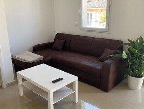 A living room with a brown leather sofa, a white coffee table, and a potted plant.