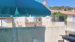 Un espace patio avec une table et des chaises, un parasol bleu et une vue sur des bâtiments en arrière-plan.