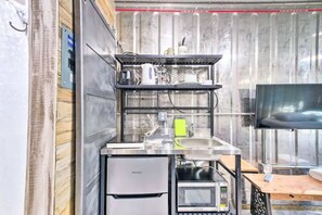 Compact kitchenette with refrigerator, microwave, and sink, featuring a flat-screen TV and ample storage.