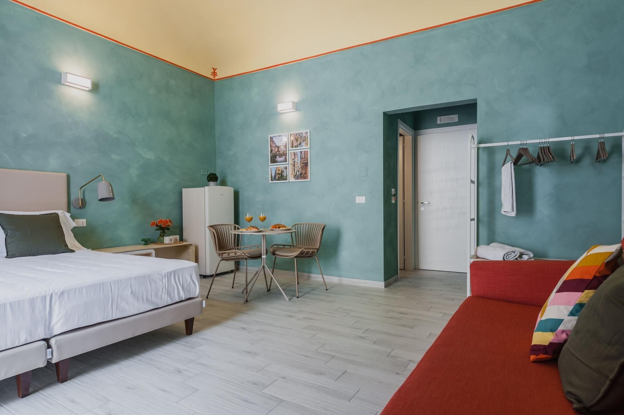 A bedroom with a bed, a small table with two chairs, a refrigerator, and a door leading to a bathroom.