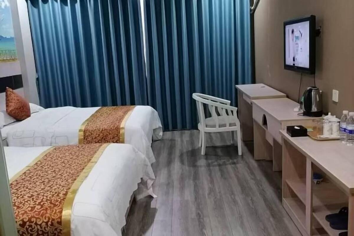 A hotel room with two beds, a desk, a chair, a television, and a curtain.