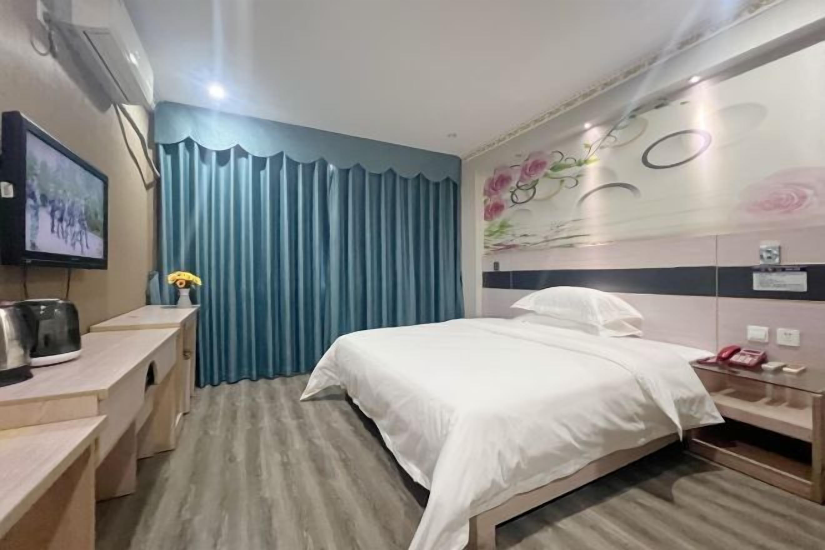 A hotel room with a bed, a desk with a kettle, a telephone, and a TV on the wall.