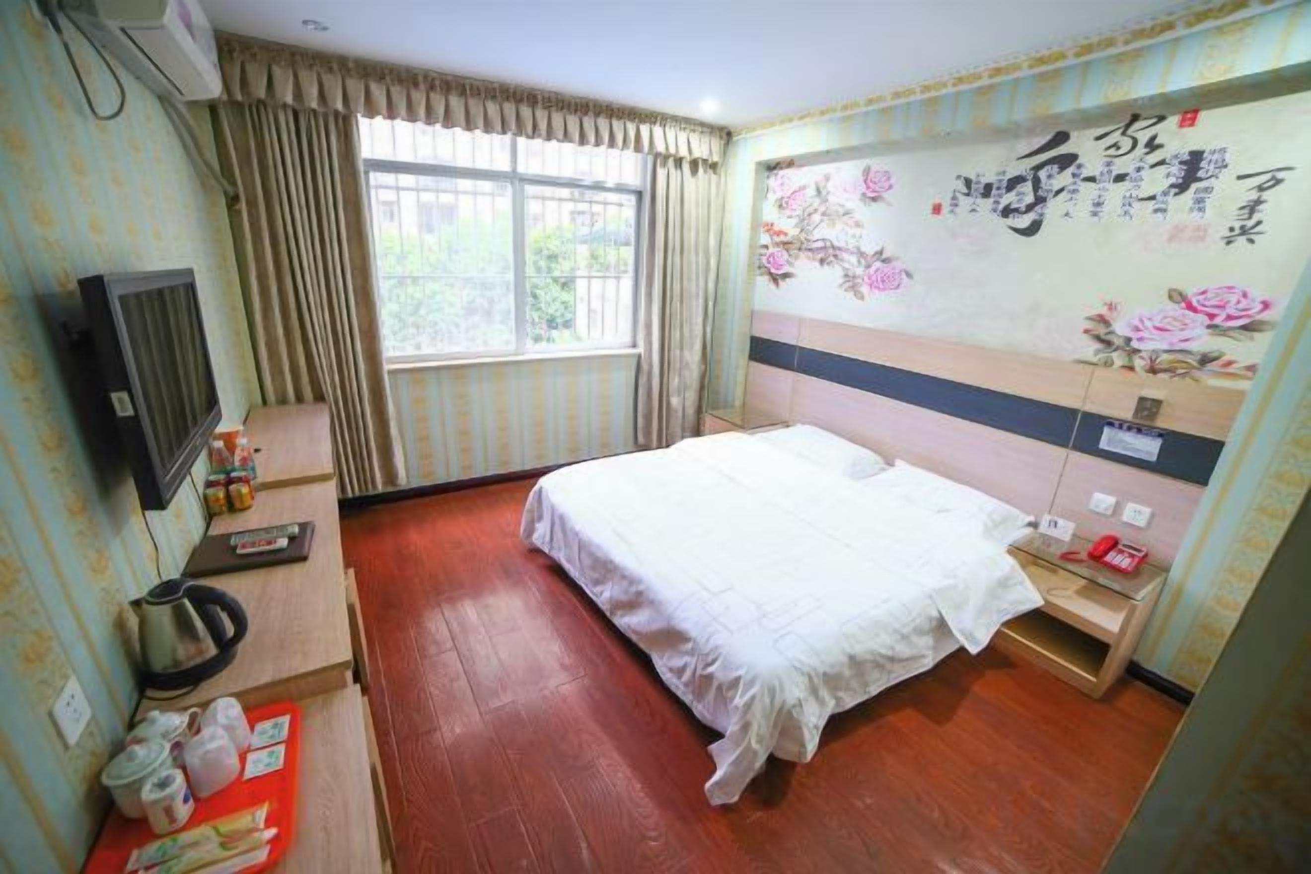 A hotel room with a bed, a television, a desk, and a window with curtains.
