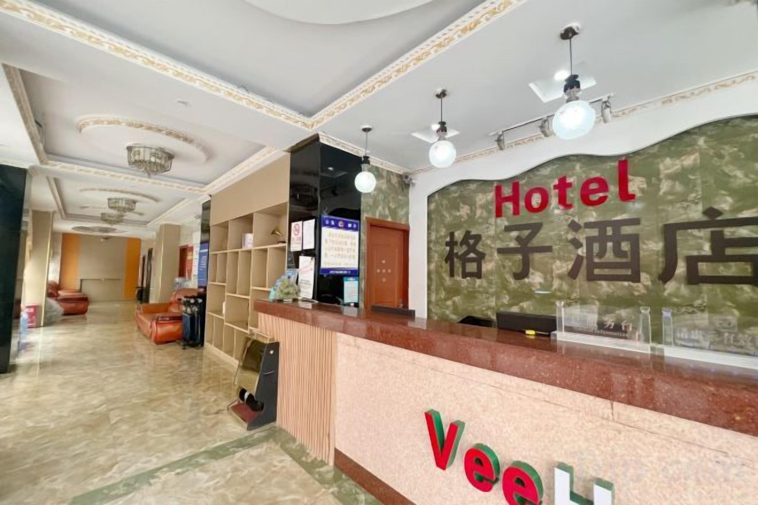 Zona de recepción de un hotel con mostrador, candelabro y una pared con el nombre del hotel en varios idiomas.