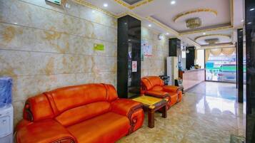 A hotel lobby with a reception desk, two leather sofas, a coffee table, and a marble floor.