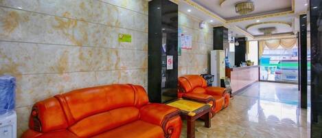 A hotel lobby with a reception desk, two leather sofas, a coffee table, and a marble floor.