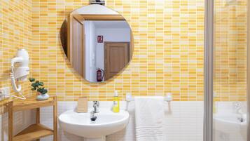 A bathroom with a yellow-tiled wall, a white sink, a mirror, and a shower area.
