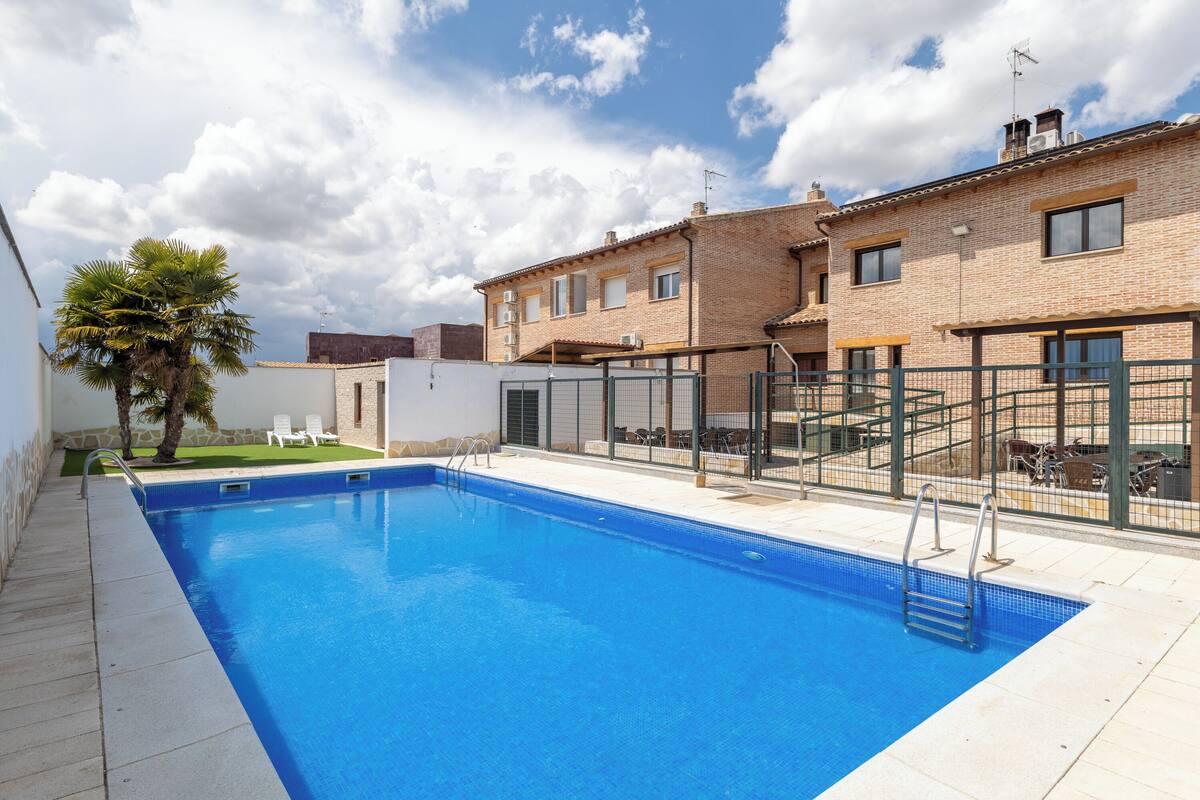 Piscina rectangular con una escalera de metal, rodeada por un solárium con baldosas.