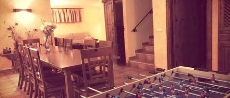 Un comedor con mesa de futbolín, sillas y una lámpara de mesa.