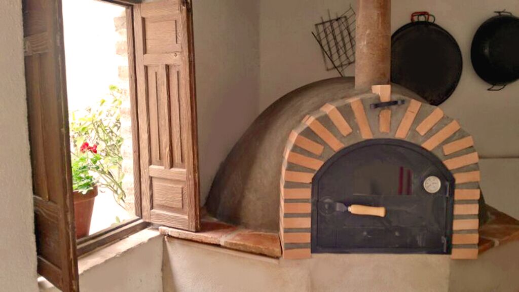 Un four en briques rustique avec une porte en bois, une plante en pot et des ustensiles de cuisine suspendus.