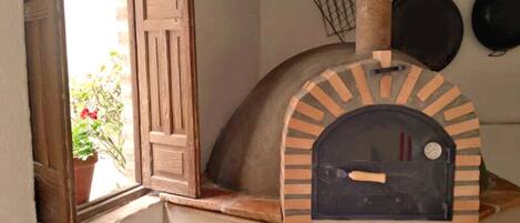 Un four en briques rustique avec une porte en bois, une plante en pot et des ustensiles de cuisine suspendus.