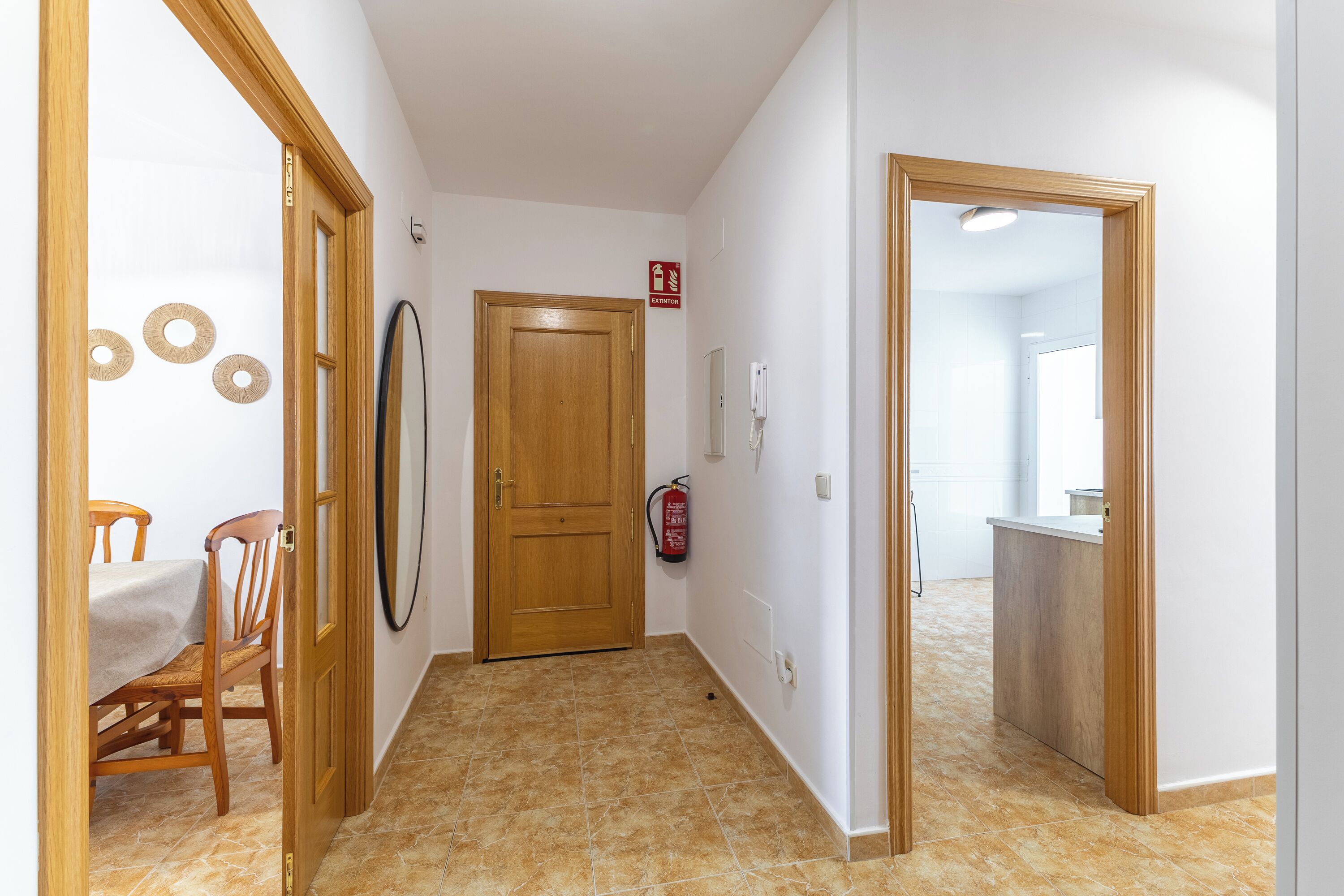 A hallway with a wooden door, a fire extinguisher, and a kitchen area visible through an open door.