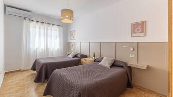 A hotel room with two beds, a wooden nightstand, a small potted plant, and a wall-mounted shelf.
