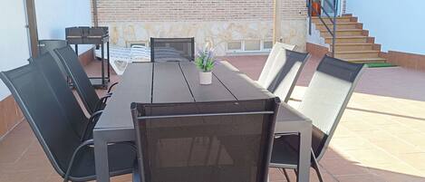 Un patio al aire libre con una mesa y sillas, una zona cubierta, un muro de ladrillo y una escalera.