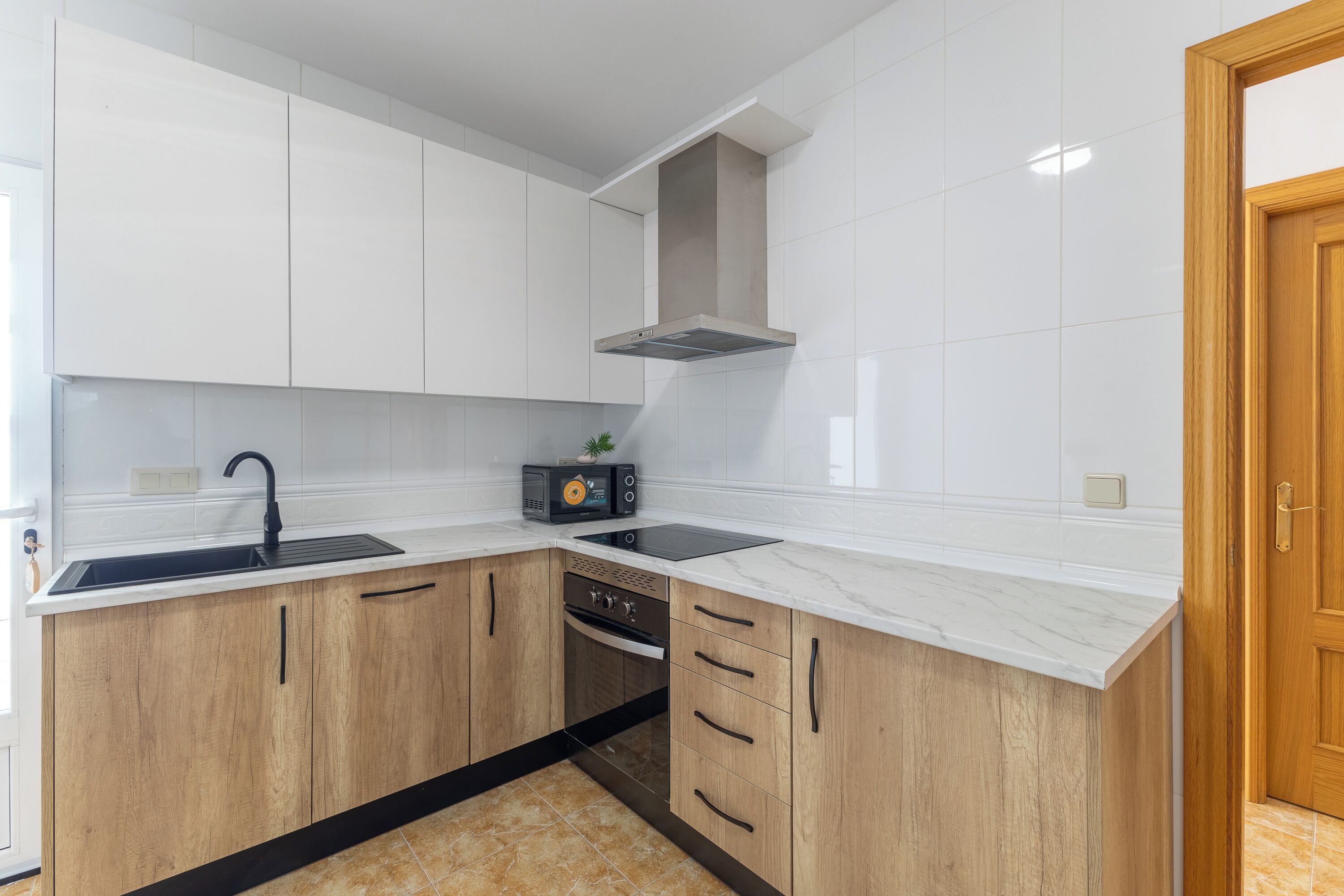 Una cucina moderna con mobili bianchi, un lavello nero, forno integrato e un piano di lavoro in legno.