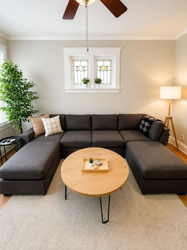 A living room with a sectional sofa, a round coffee table, a ceiling fan, a window with stained glass, and a floor lamp.