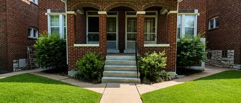 A two-story brick building with a central entrance, a covered porch, and a symmetrical facade.