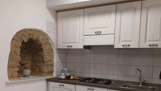 Een keuken met witte kastjes, een stenen boog, een gasfornuis en een spoelbak.