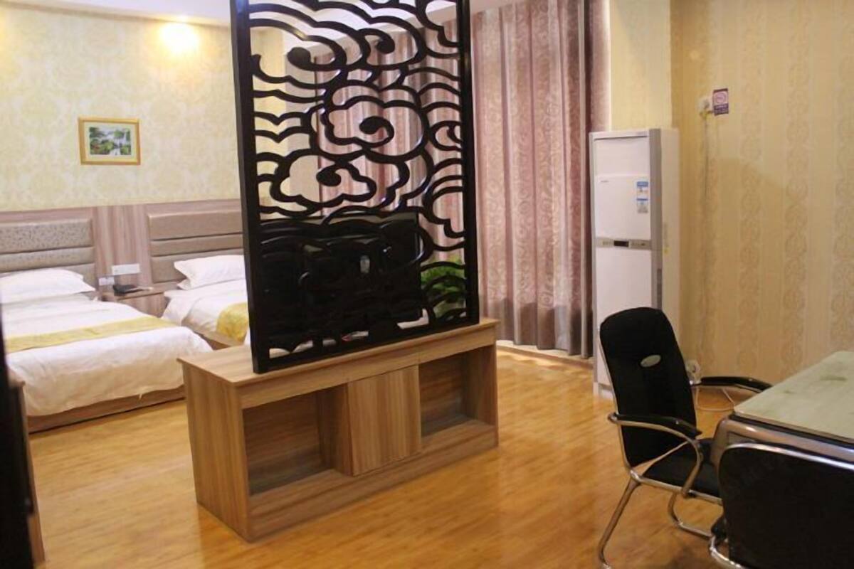 Habitación de hotel con dos camas, un mueble bajo de madera para la televisión, un refrigerador y un área de comedor con una silla.