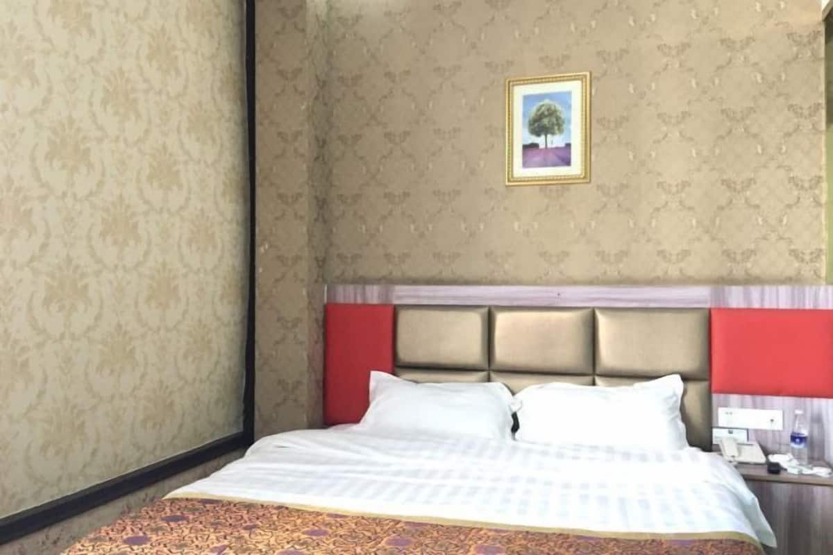 Habitación de hotel con cama, cabecero, mesita de noche y un cuadro en la pared.