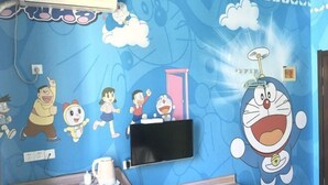 A room with a blue wall featuring cartoon characters, a flat-screen TV, a small table with a cup, and a door. - Yilu Tongxing Chain Hotel (Suixi)