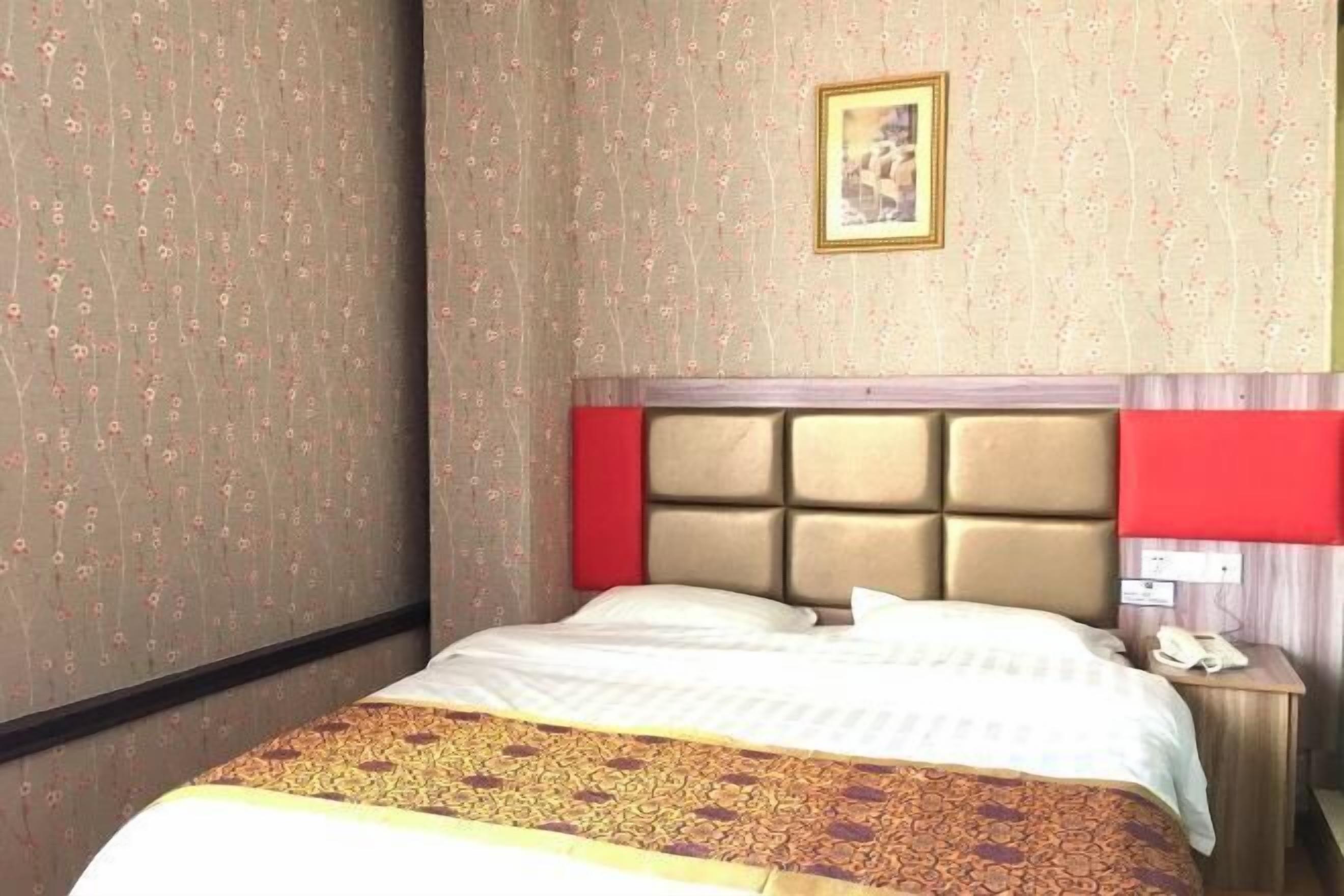 A hotel room with a bed, a nightstand, a telephone, and a framed picture on the wall.