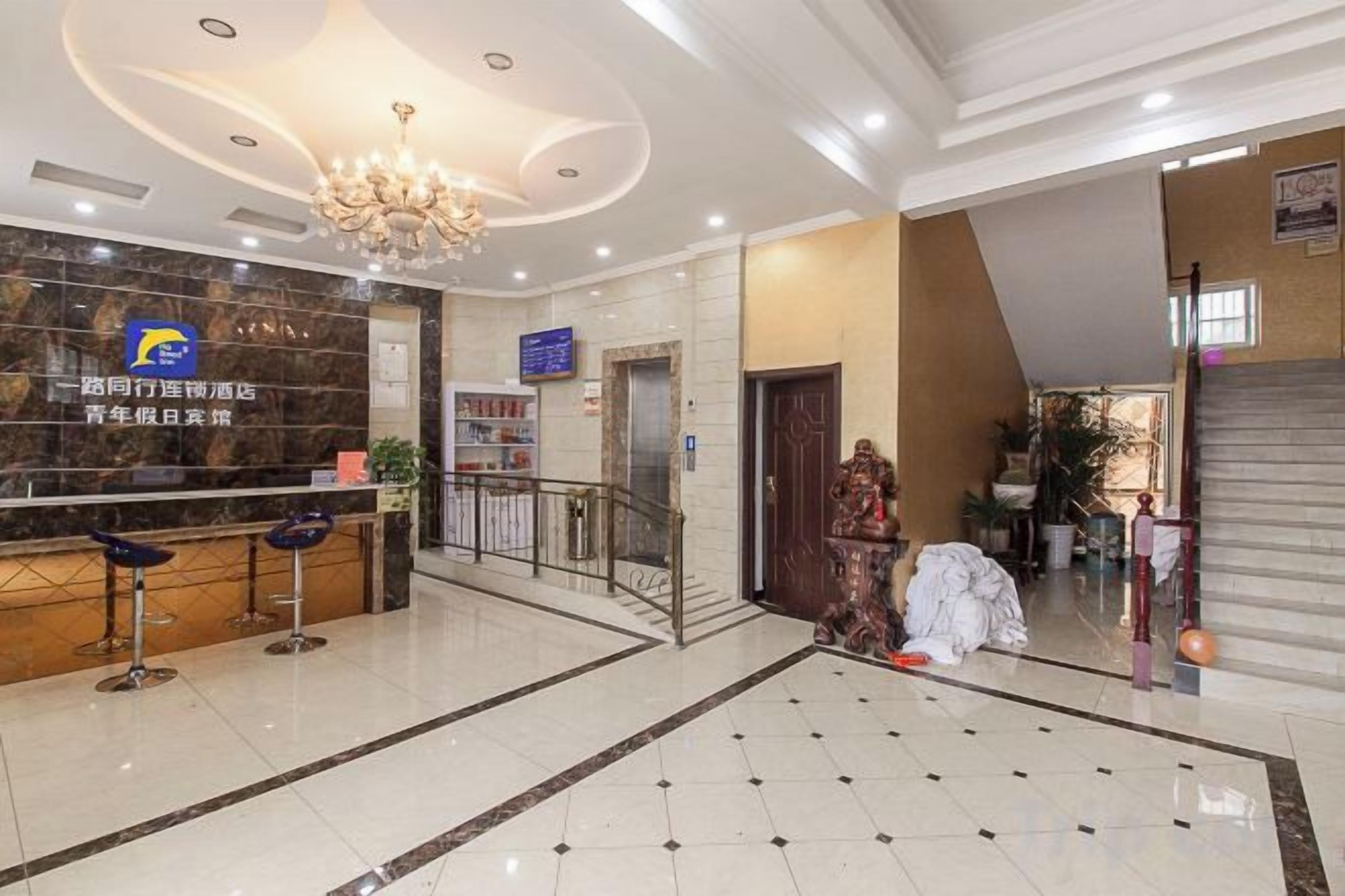 A hotel lobby with a reception desk, a chandelier, a staircase, and a large tiled floor.