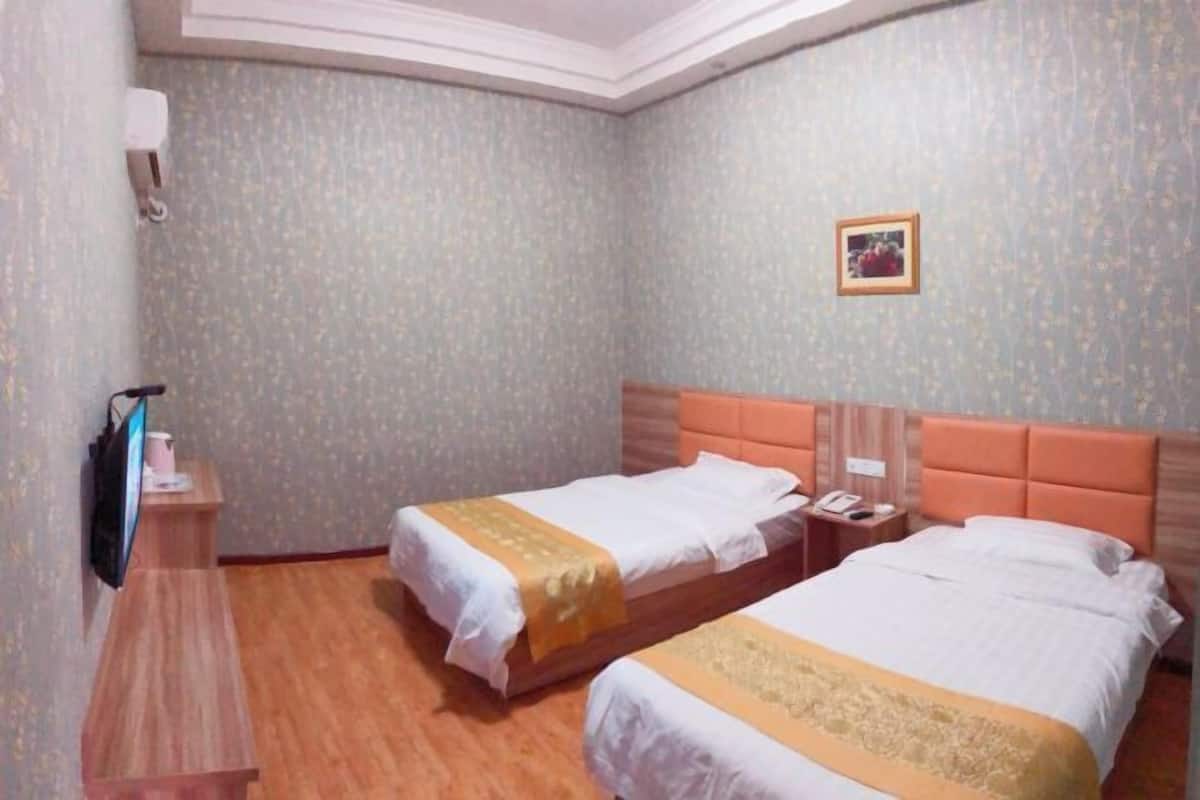 Habitación de hotel con dos camas, un escritorio pequeño con una computadora y un televisor montado en la pared.