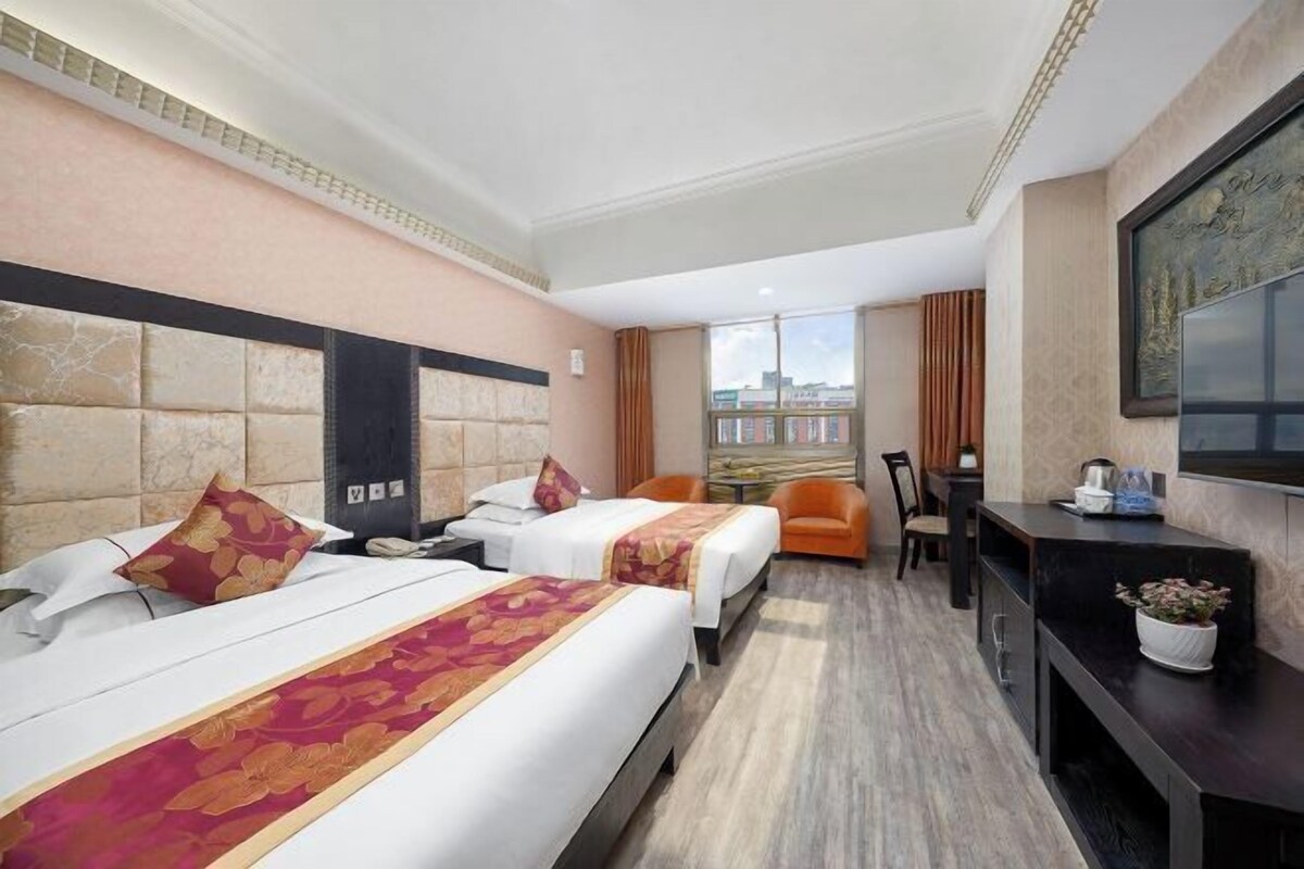 A hotel room with two beds, a desk, a chair, a TV, and a window with a city view.
