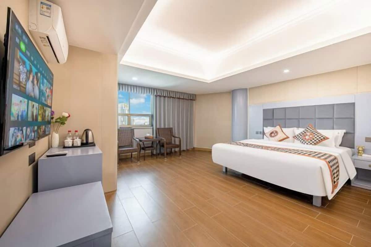 A hotel room with a bed, bedside table, TV, and a seating area with chairs and a table.
