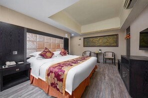 A hotel room with a large bed, a nightstand, a desk, two chairs, and a painting on the wall. - Jinman Island Hotel (Shenzhen Qinghu Subway Station Branch) (Shenzhen)