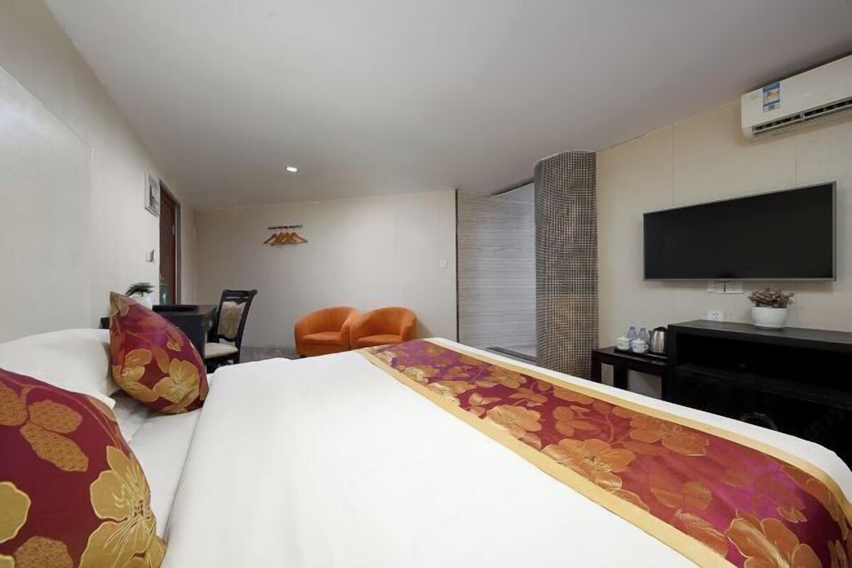 A hotel room with a bed, two chairs, a TV, and a wall-mounted air conditioner.