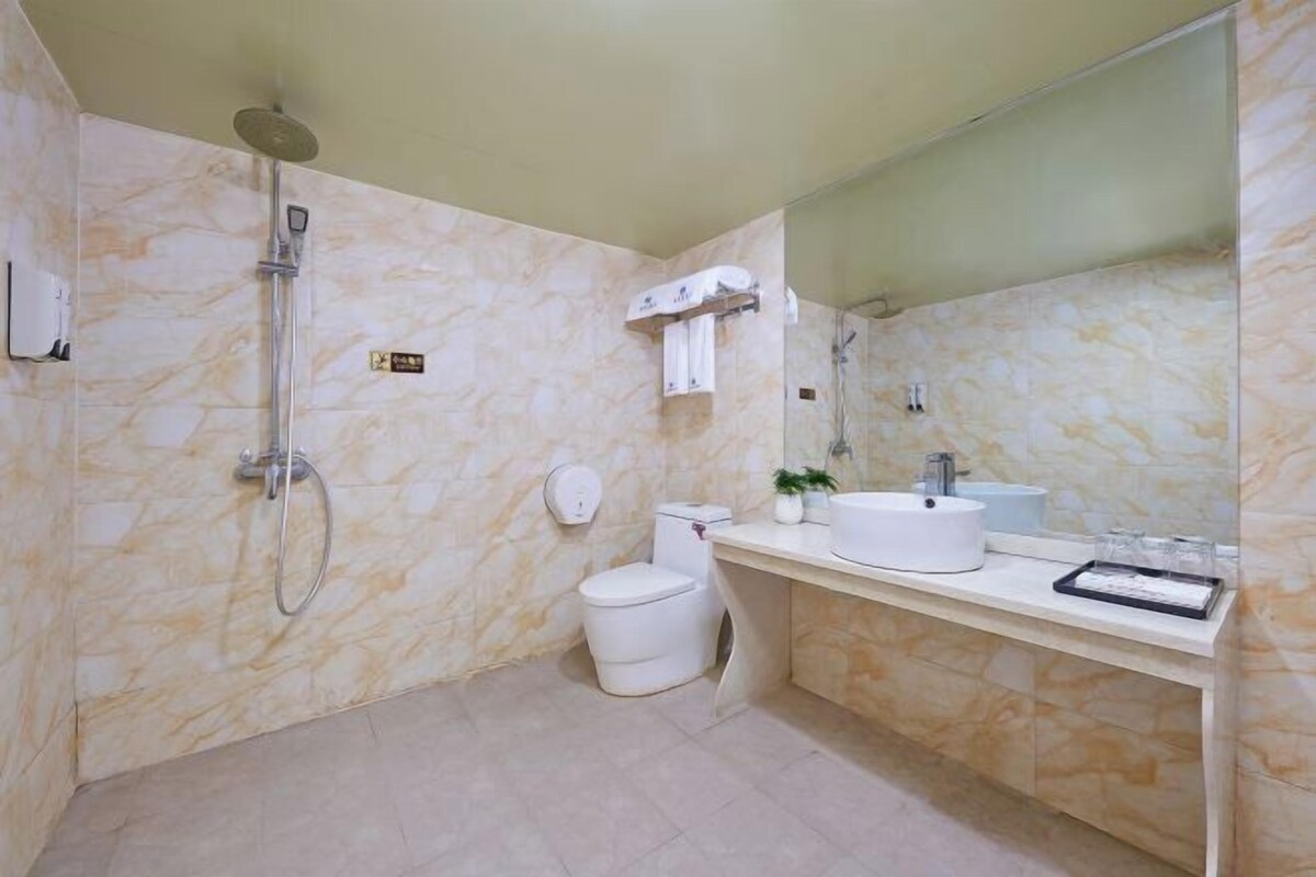 A bathroom with a marble wall, a toilet, a sink, a mirror, and a shower.