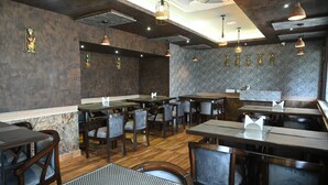 Interior de un restaurante con mesas y sillas de madera, y lámparas colgantes.